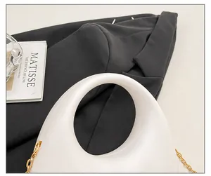 Detail der weißen Beuteltasche mit rundem Griff und goldener Schulterkette