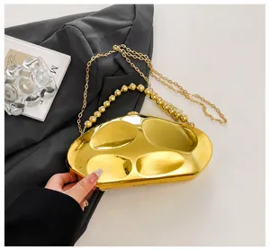 Dettaglio borsa da sera dorata a specchio con design a fagiolo e manico di perle