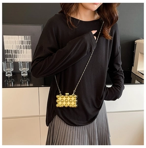 Detailopname van de gouden acryl box bag met 3D-bubbeltextuur en dunne metalen ketting