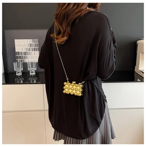 Achteraanzicht van een model met een gouden mini kettingtas met bubbeltextuur als sieraad