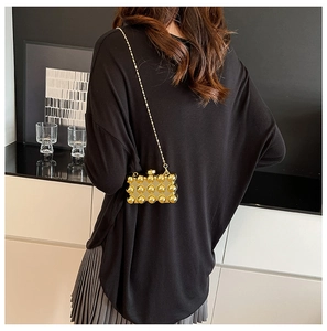 Detail van gouden mini-kettingtas met 3D metalen boltextuur op zwarte kleding