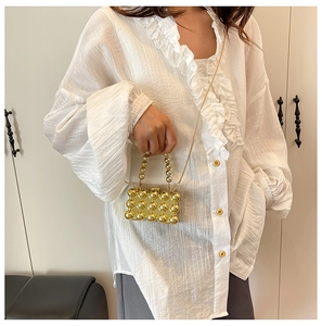 Detail van een gouden mini box tas met kralen, metalen handvat en ketting riem