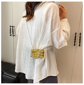 Detail van een mini gouden acryl crossbody tas met grote kralen en metalen ketting