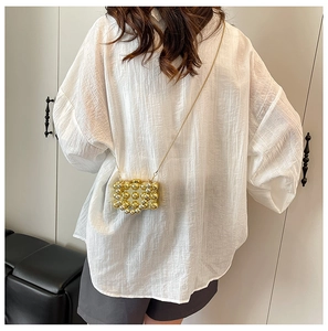 Achteraanzicht van model met een gouden bolvormige tas en een fijne metalen ketting