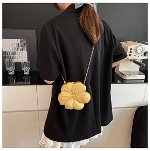 Detail of golden 3D flower clutch bag with metal chain strap worn by a model