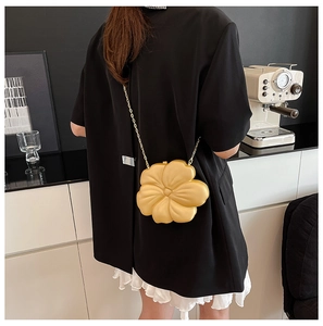 Close-up of a 3D yellow flower clutch bag with gold chain strap on a black outfit
