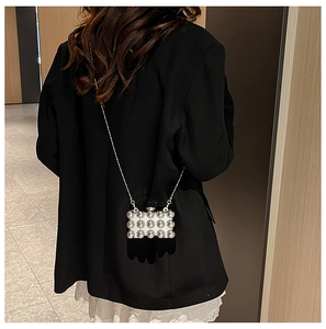 Detail van een mini-acryl parel crossbody tas met zilveren ketting op zwarte blazer