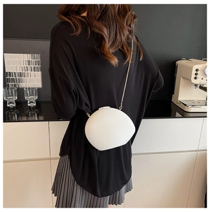 Minimalist white pebble-shaped shell crossbody bag with a slim gold chain on a female model