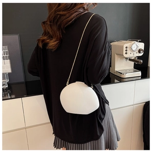 Detail of white pebble-shaped crossbody bag with elegant gold chain strap on a model