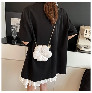 Detail showing white flower-shaped evening bag with gold chain strap on shoulder