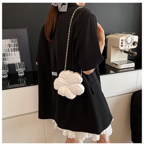 Detailed side view of a white flower-shaped crossbody bag with gold chain strap on model