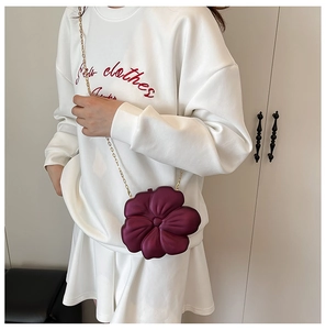 Detail of burgundy flower-shaped clutch bag with golden chain strap on a model