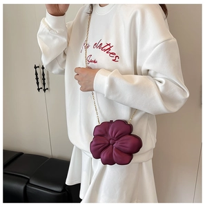 Detail of burgundy flower-shaped evening clutch with gold chain on model in white sweatshirt
