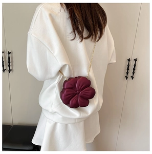 Burgundy flower evening bag with gold chain strap worn by model against a neutral wall