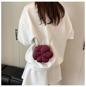 Detail of burgundy flower-shaped clutch bag with golden chain on white dress