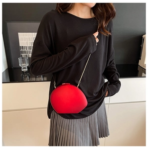 Detail of red shell-shaped crossbody bag with gold chain strap on a model