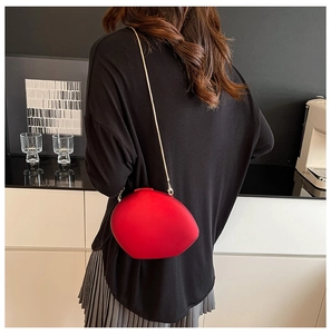 Detail of red shell-shaped acrylic crossbody bag with gold chain strap on model