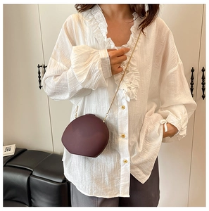 Chic burgundy pebble shaped crossbody bag with gold chain strap on a white blouse