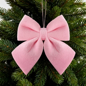 Close-up of pink velvet Christmas bow ornament hanging on a lush green pine branch