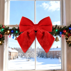Large red velvet Christmas bow hanging on a wreath with snowy window background