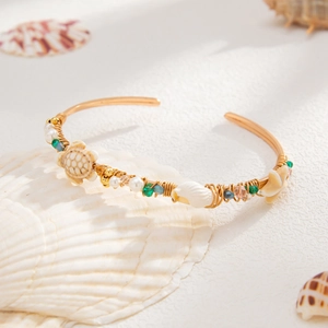 Bohemian gouden bovenarmband met zeeschildpad, zeester en parels op wit zand achtergrond
