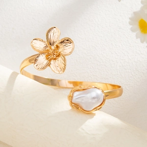 Λεπτομέρεια χρυσού βραχιολιού με μεταλλικό λουλούδι και ένα μπαρόκ μαργαριτάρι