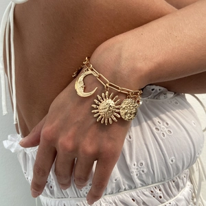 Close-up of gold charm bracelet with sun and moon pendants on a model wrist