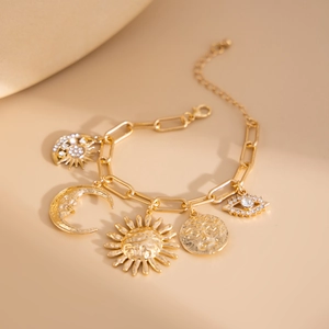 Detailed close-up of gold paperclip chain bracelet with sun, moon and eye charms