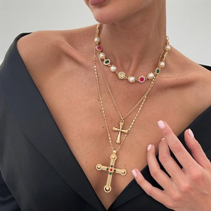 Gelaagde gouden ketting met kruis, parels en kleurrijke edelstenen op een model