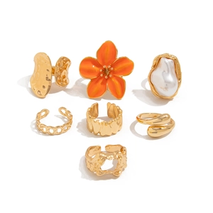 Set van 7 gouden ringen met oranje bloem, barokke parel en metalen ringen met textuur