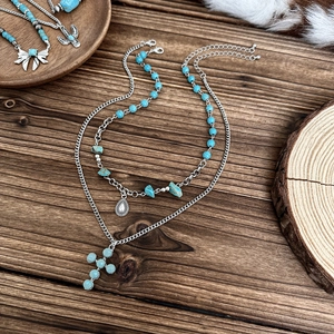 Detail of layered turquoise cross pendant necklace with silver teardrop charms on dark wood