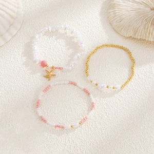 Three-piece starfish and pearl beaded bracelet set with ocean theme on sand background