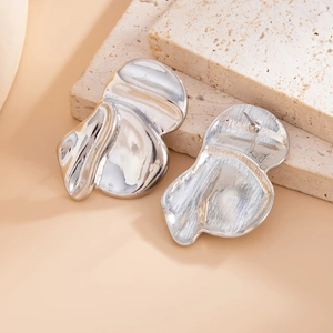 Dettaglio di orecchini irregolari in metallo argento con texture su pietra beige