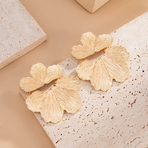 Dettaglio degli orecchini a fiore dorati con texture spazzolata su pietra