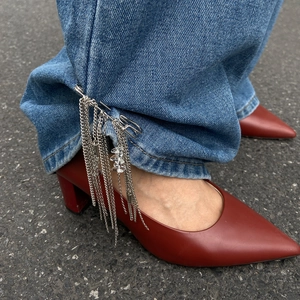Detail of silver layered rivet chain anklet with tassels on denim and red high heels