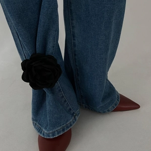 Detail of a chic 3D black fabric rose brooch clipped on blue denim jeans hem