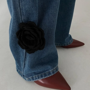 Blue denim pants featuring large 3D black fabric rose tassel detail at the ankle cuff