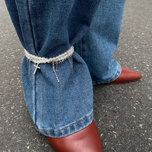 Detail einer zweilagigen Perlen-Fußkette mit Kristallkreuz und Quaste am Denim-Saum