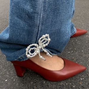 Detail of beaded pearl bow clip on denim jeans paired with red pointed-toe shoes