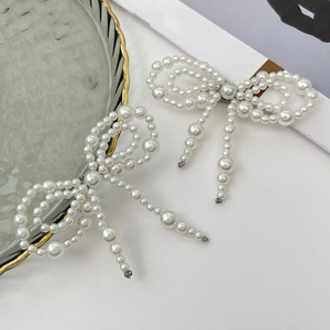 Elegant white faux pearl bow hair clip set with gold metal clasp on a minimal white surface