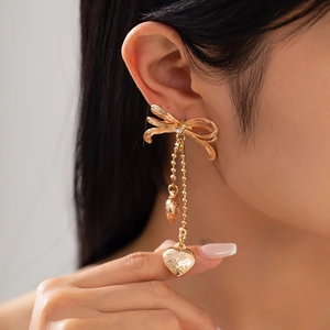 Boucles d'oreilles nœud dorées avec pendentifs cœur et glands sur un mannequin