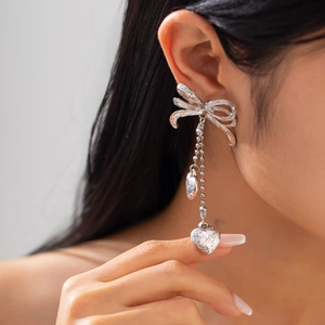 Détail de boucles d'oreilles nœud argentées avec pompons perlés et cœurs sur un modèle