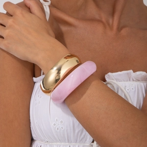 Detail of wide gold metal bangle paired with pink marbled resin bracelet on wrist
