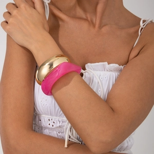 Close-up of stacked metallic gold wide cuff and magenta wavy resin bangle on wrist