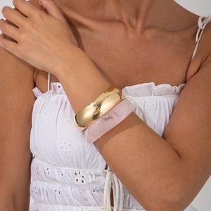 Detail of pink marble resin bangle and gold metal bracelet on a model wrist