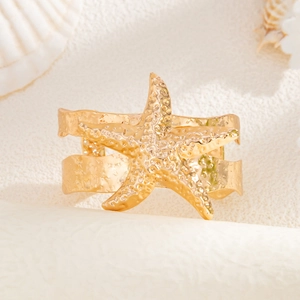 Makroaufnahme einer goldenen Seestern-Manschette mit Hammerschlag-Textur auf Sand