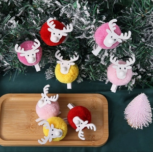 Close-up of colorful plush elk photo clips on snow-covered pine branches for Christmas decor