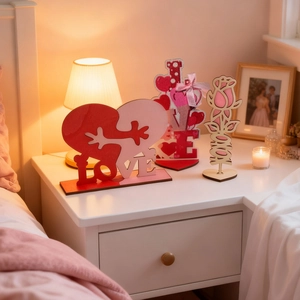 Nahaufnahme von drei Valentine Holzdeko LOVE Herz und Rosen Tischornamenten auf dem Nachttisch