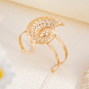 Detailansicht eines goldenen Nautilus-Anhängers an einem offenen Armreif im Strandstil