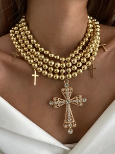 Détail d'un collier de perles dorées à plusieurs rangs avec pendentifs croix en cristal